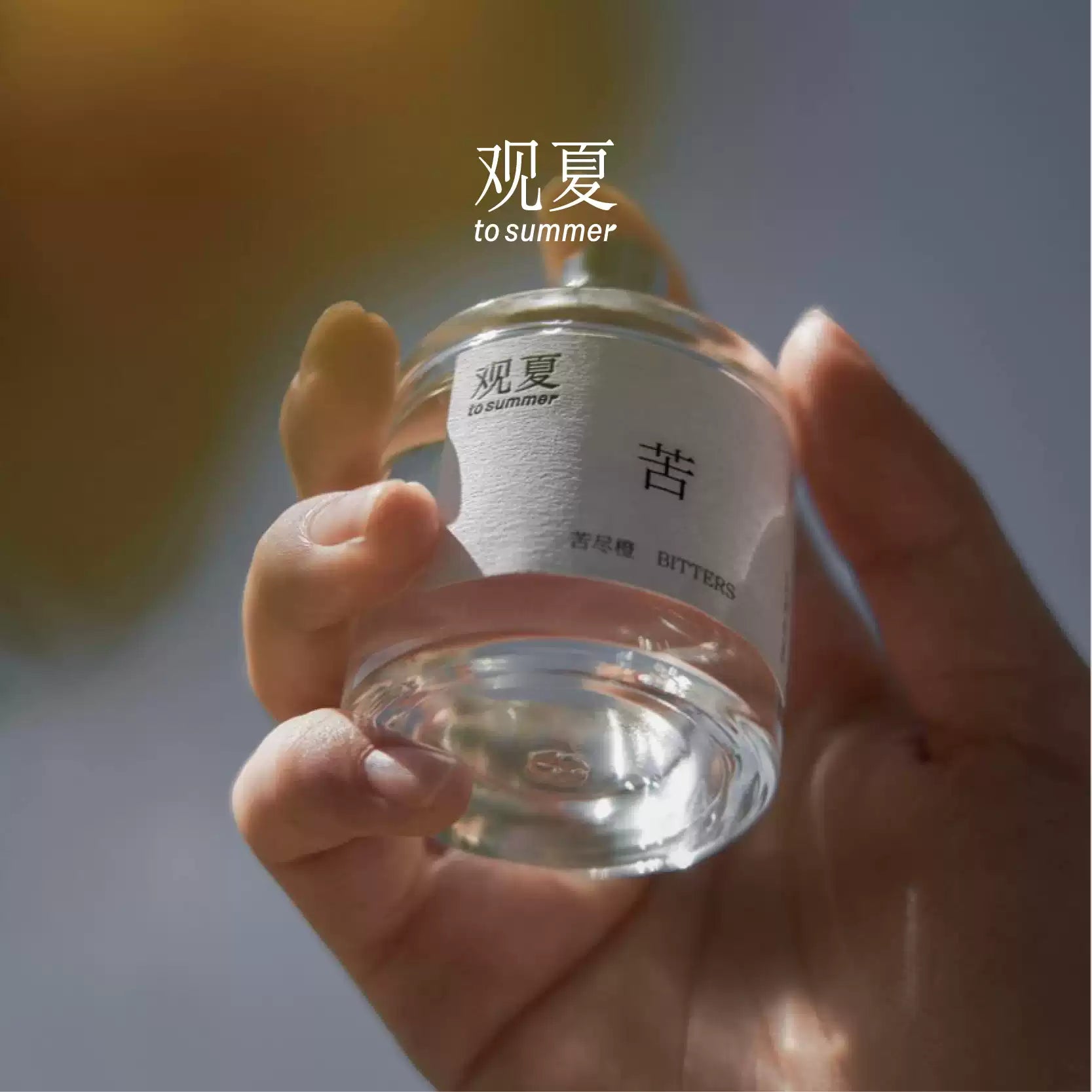 Hand holding To Summer BITTERS perfume in warm sunlight, showcasing the fresh and uplifting citrus notes.