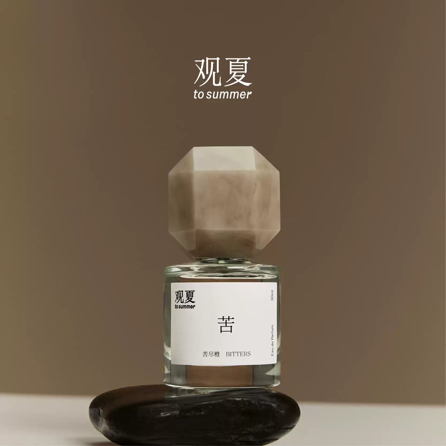 To Summer BITTERS perfume bottle balanced on a zen stone, symbolizing resilience and grounding energy.