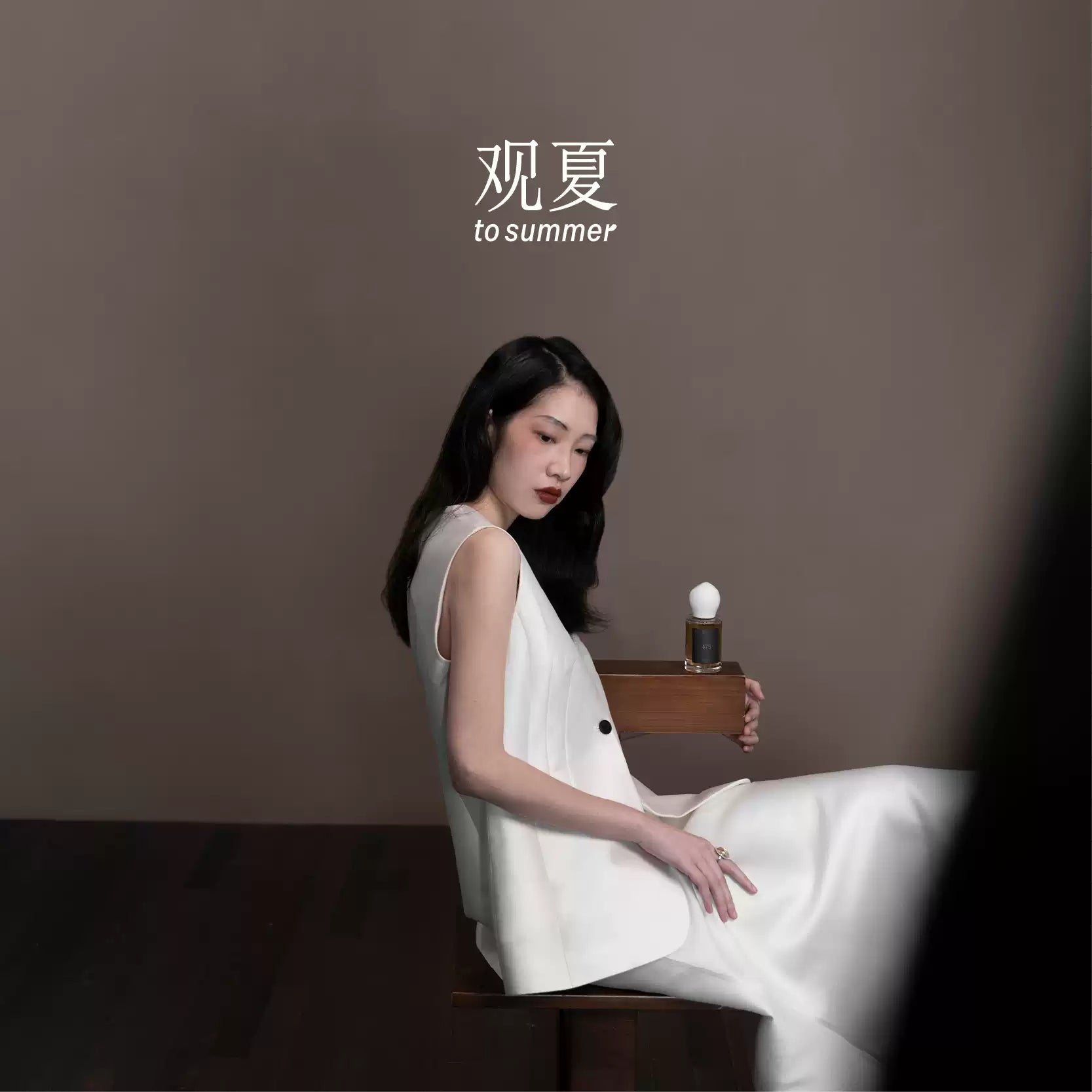 Elegant woman in white dress posing with To Summer 475 MANSION perfume, showcasing luxury fashion style.