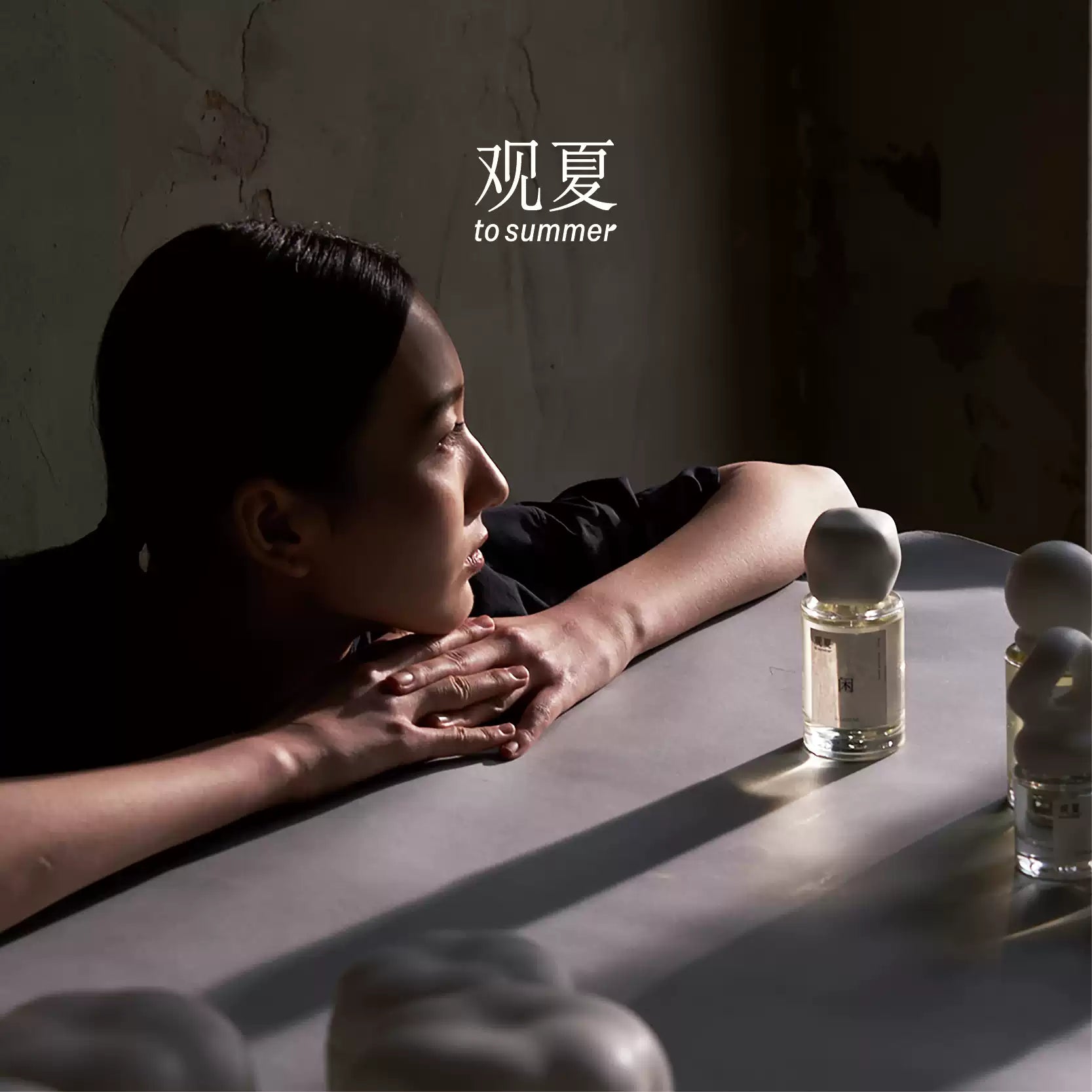 Woman gazing at To Summer LEISURE perfume in soft light, evoking a meditative and calming mood.