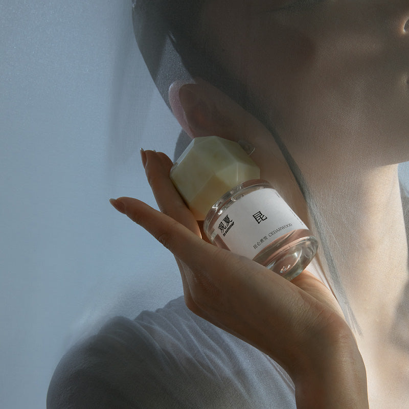 To Summer Cedarwood perfume bottle on a reflective surface surrounded by clear liquid, creating a pure and natural calm aesthetic.