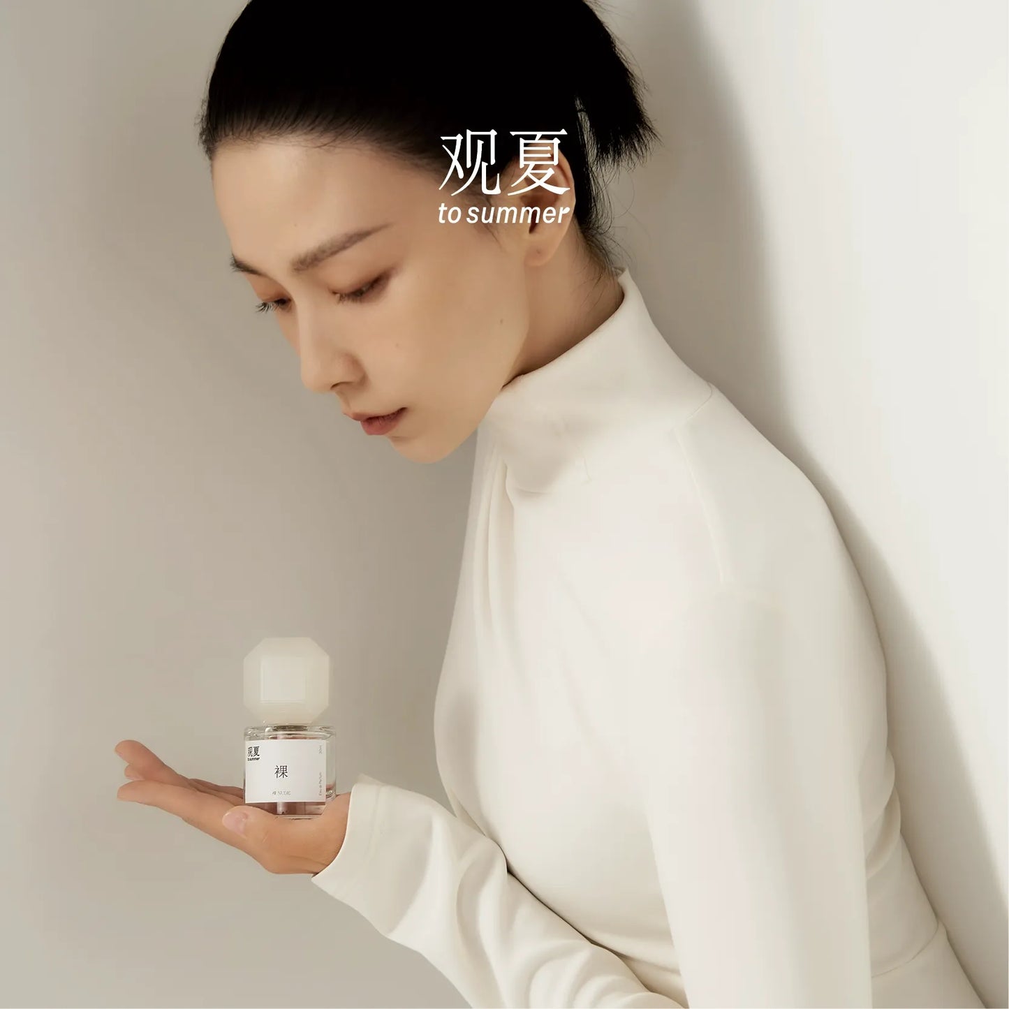 Woman in white turtleneck holding To Summer NUDE perfume, representing the scent of pure white musk.