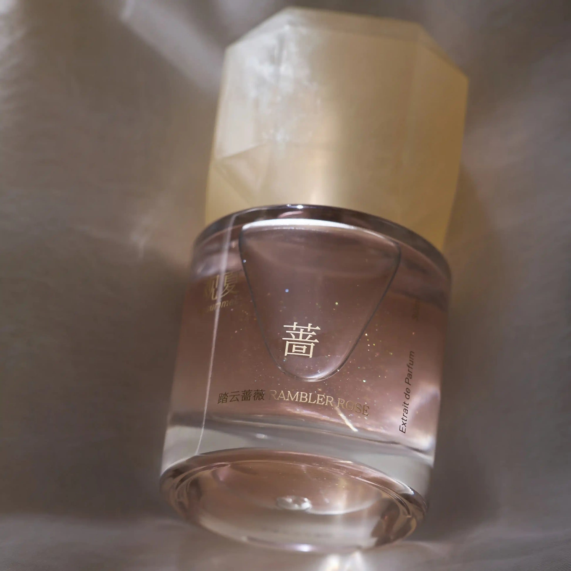 Close-up of RAMBLER ROSE perfume bottle, highlighting a green floral rose fragrance with warm amber base