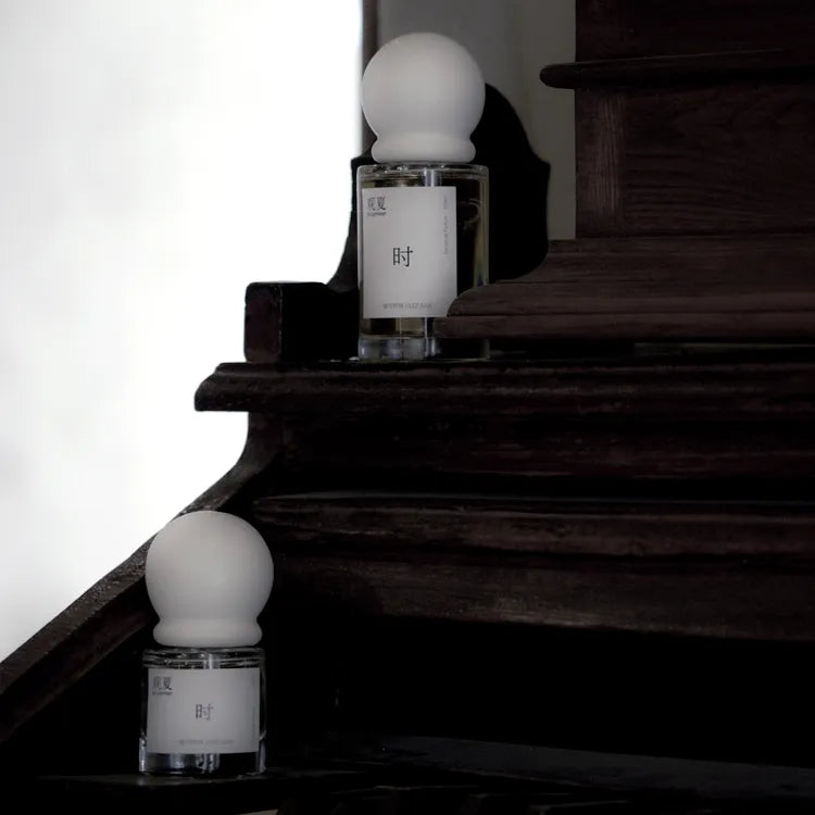 Two sizes of To Summer JAZZBAR perfume placed on a dark wooden staircase, symbolizing nostalgia and timeless style.